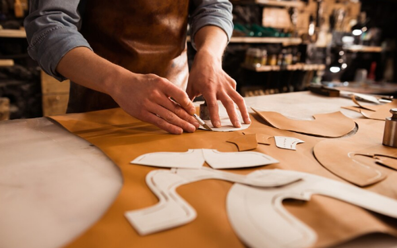 a shoemaker measuring and cutting leather